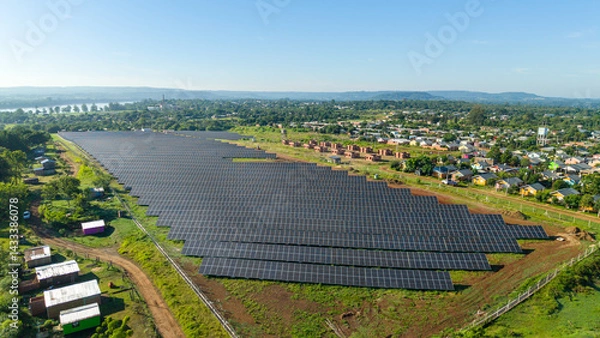 Fototapeta Extensive field of solar panels seen from above, surrounded by houses and trees in a rural environment.
