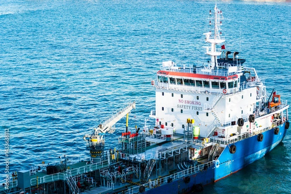 Fototapeta Close-up aerial view on the tanker ship, fuel bunker barge in the container terminal, she is arriving to supply large cargo ship with fuel oil. 