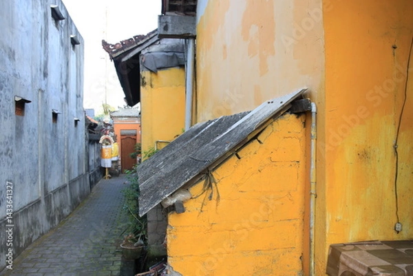 Fototapeta Yellow building with a roof and a brick wall. The building is in a narrow alleyway