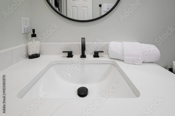 Fototapeta A bathroom sink counter displays a soap bottle, neatly folded towel, and face cloth