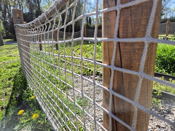 Fototapeta Close-up view of a small fence made of wooden posts and rope mesh