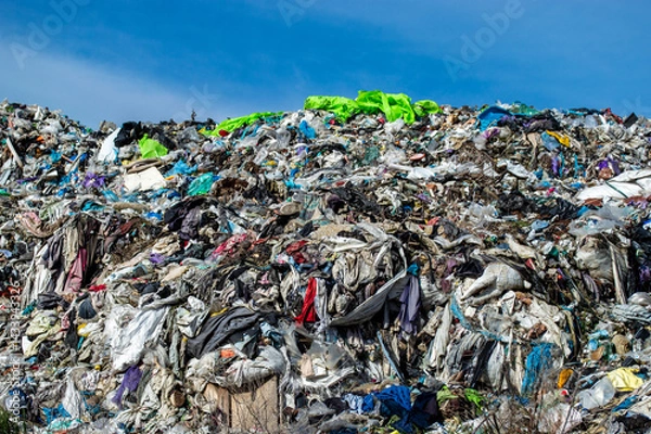 Obraz A vast accumulation of discarded clothing and fabrics fills the landfill, highlighting the issue of textile waste under bright sunlight