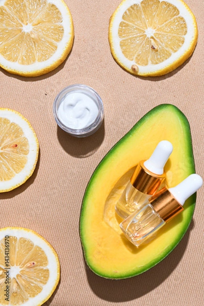 Fototapeta Two transparent skincare dropper bottles with golden caps placed inside a fresh avocado half, surrounded by green leaves on textured beige background. Natural beauty and organic skincare concept