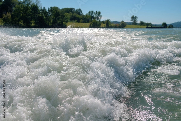 Fototapeta White motorboat tracks on the waves with a blurred green hills on the horizon