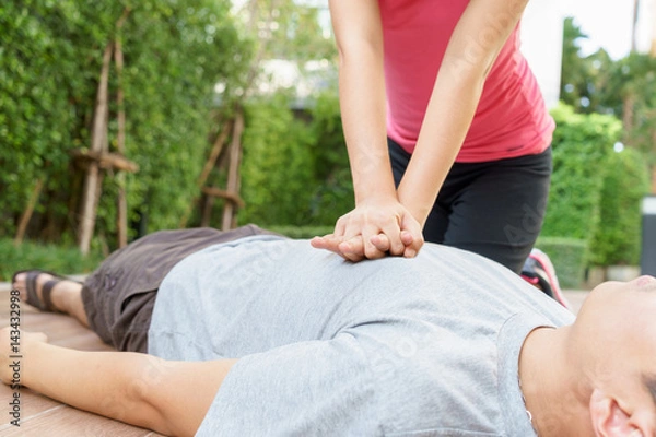 Obraz Woman giving cardiopulmonary resuscitation (CPR) to a man at public park.