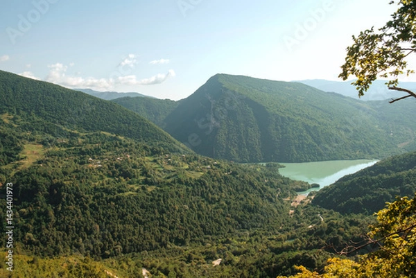 Fototapeta View of a green lake between forest covered mountains.