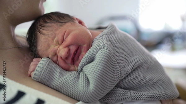 Fototapeta Newborn baby resting on mother's chest, visibly uncomfortable, expressing displeasure with a scrunched-up face. the tender moments of caring for a newborn in distress-SD 480p