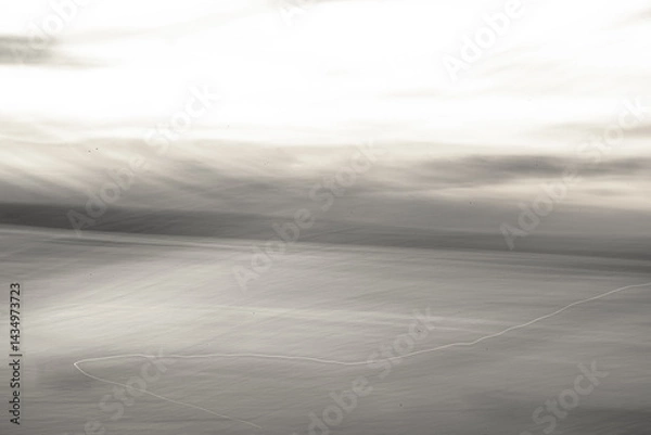 Fototapeta Camera movement creates an abstract black and white image of a tranquil coastline.
