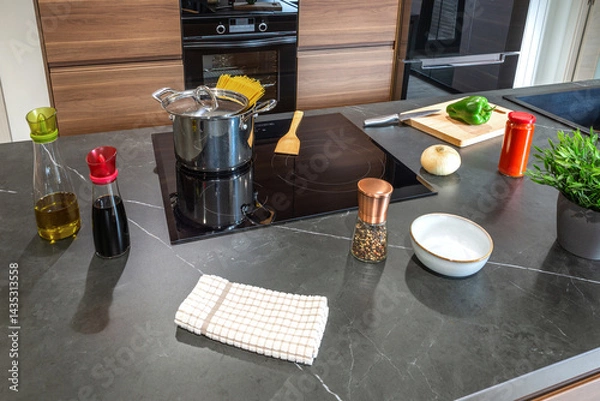 Fototapeta Ingredients for cooking spaghetti arranged on modern kitchen counter. Olive oil, soy sauce, salt, pepper, onion, green pepper, tomato sauce, spaghetti and pot near an induction hob ready for cooking