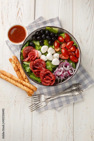 Fototapeta Pizza salad tosses mix of romaine lettuce, sausages, mozzarella, black olives and red onion in a fresh, grated tomato vinaigrette closeup on the plate on the wooden table. Vertical top view from above