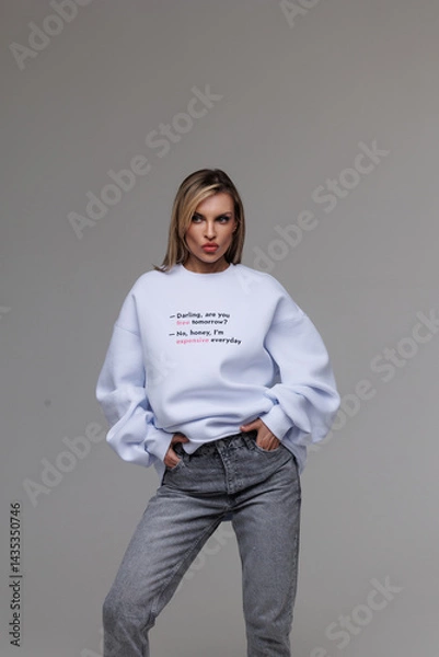 Obraz Girl in a white sweatshirt on a gray background. Commercial advertising of a sweatshirt for sale. Soft, pleasant to the body material of clothing. Beautiful brunette with long hair