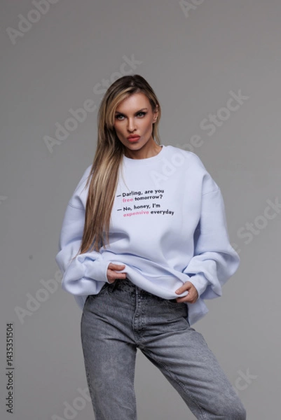 Fototapeta Girl in a white sweatshirt on a gray background. Commercial advertising of a sweatshirt for sale. Soft, pleasant to the body material of clothing. Beautiful brunette with long hair
