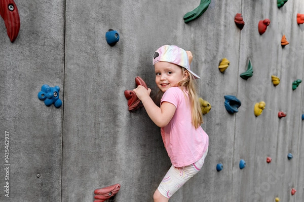 Fototapeta Little happy child climbing on a climbing wall on a playground in summer. Physical education at school or kindergarten. Concept of sports and healthy lifestyle.