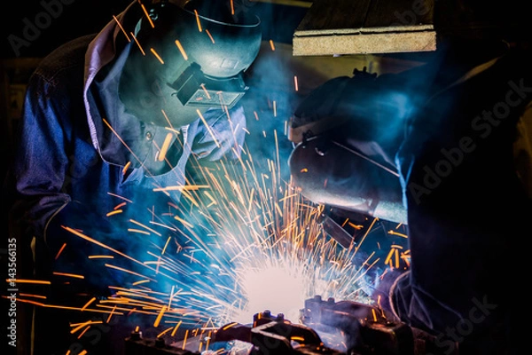 Fototapeta Team welder are welding metal part in factory

