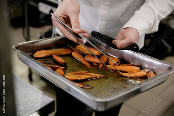Fototapeta Cropped unrecognizable person getting tray with honey glazed carrots out of oven