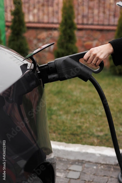 Obraz Unrecognisable woman inserting EV charger plug from public or home charging station for modern electric or hybrid car at special place for e-car. Concept eco-friendly sustainability energy car