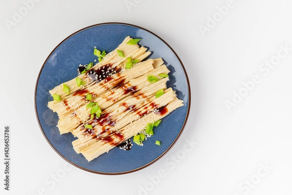 Fototapeta Tofu skin or yuba with green onions, sauce and sesame seeds in a blue plate.  Asian dish isolated on white background