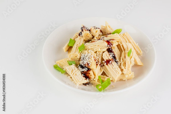 Fototapeta Tofu skin or yuba with green onions, sauce and sesame seeds in a white plate.  Asian dish isolated on white background