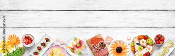 Obraz Summer garden party food bottom border. Assortment of fun flower theme charcuterie items, cheese, fruit, vegetables and finger snacks. Top down view on a white wood banner background.