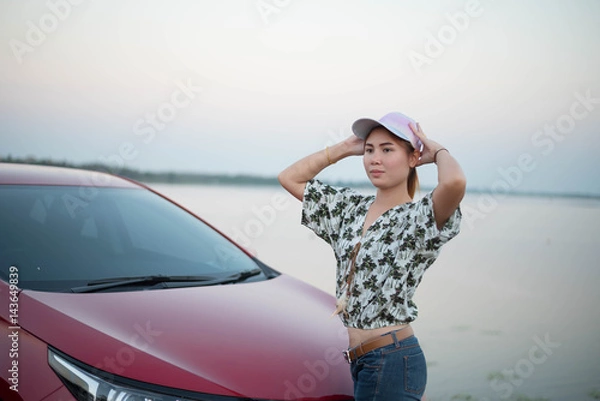 Fototapeta young woman standing in front of the red car with sunset on the park