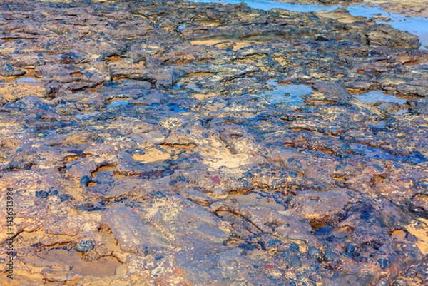 Obraz Rocky terrain with puddles of water, suggesting a coastal or tidal area. Contrasting textures of wet and dry rocks, along with their varied colors, create a visually compelling and dynamic scene