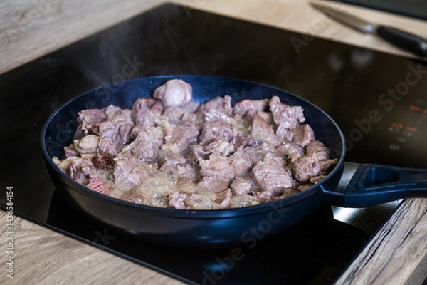 Fototapeta Close up of meat cooking in a frying pan with steam. A frying pan on an induction cooker preparing meat for Pilaf. Cook recipe step-by-step.