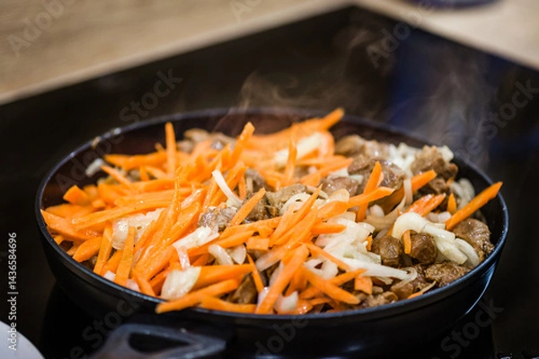 Fototapeta A frying pan on an induction cooker preparing carrots, meat and onions.  Cook recipe step-by-step. Pilaf recipe in pictures.