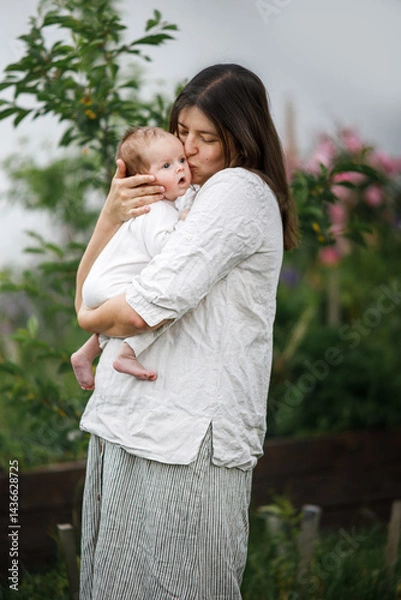 Fototapeta Happy Mothers day! Mother kissing and hugging cute newborn baby  in the garden. Love, care and family in countryside concept. Adoption and maternity