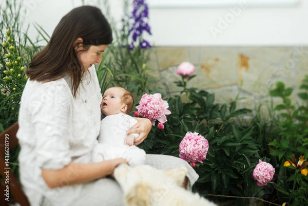 Fototapeta Happy Mothers day! Mother hugging cute newborn baby among flowers in the garden. Love, care and family in countryside concept. Adoption and maternity