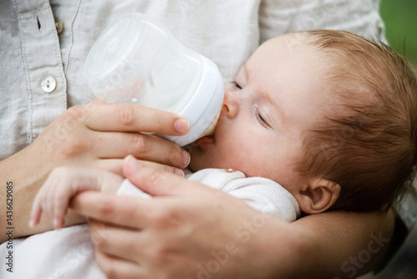 Fototapeta Mother feeding cute newborn baby with bottle close up in the garden. Love, care and family in countryside concept. Happy Mothers day! Adoption and maternity