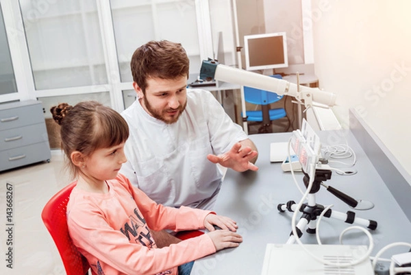 Obraz Orthoptics. Pleoptics. Doctor explains how to use ophthalmic equipment. Eye training. Vision rehabilitation.