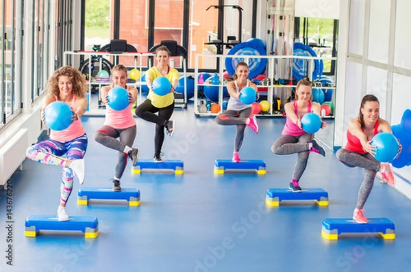 Fototapeta Group of beautiful young women working out on blue stepper and smiling.