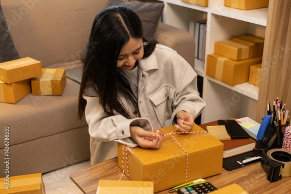 Fototapeta A woman is holding two boxes and smiling. She is sitting in front of a laptop. The boxes are brown and appear to be gifts. The woman seems happy and excited about the boxes
