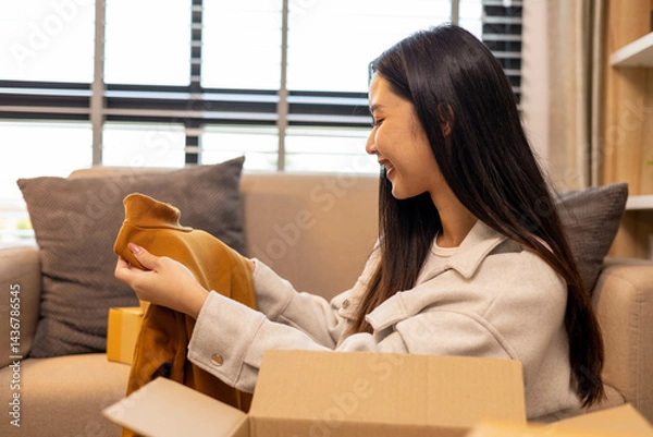 Fototapeta A woman is holding two boxes and smiling. She is sitting in front of a laptop. The boxes are brown and appear to be gifts. The woman seems happy and excited about the boxes
