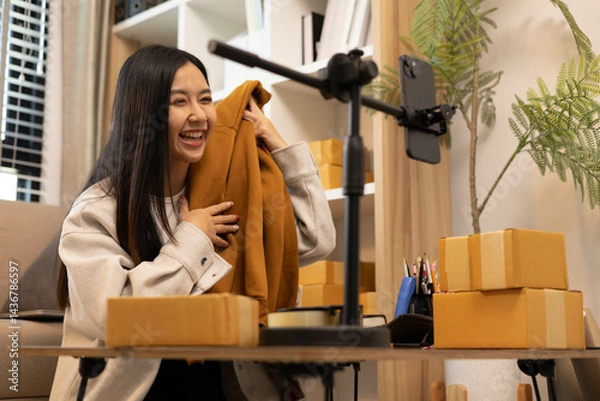 Fototapeta A woman is holding two boxes and smiling. She is sitting in front of a laptop. The boxes are brown and appear to be gifts. The woman seems happy and excited about the boxes
