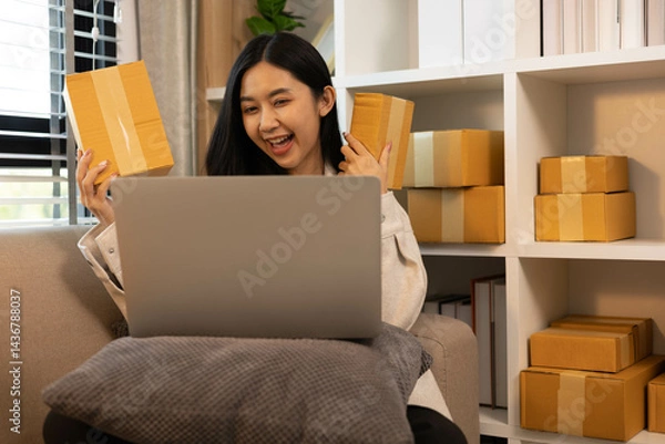 Fototapeta A woman is holding two boxes and smiling. She is sitting in front of a laptop. The boxes are brown and appear to be gifts. The woman seems happy and excited about the boxes

