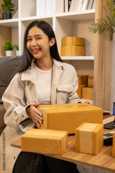 Fototapeta A woman is holding two boxes and smiling. She is sitting in front of a laptop. The boxes are brown and appear to be gifts. The woman seems happy and excited about the boxes
