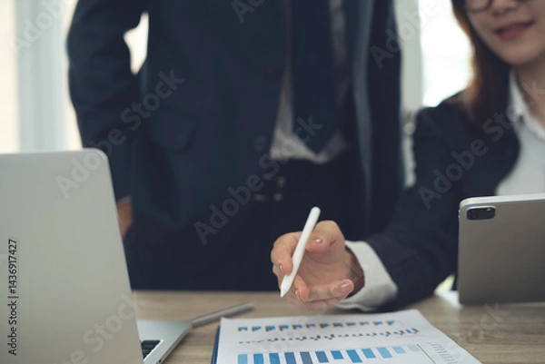 Fototapeta Two business person having a discussion, analyzing business report with financial document on office table. Asian business team using laptop and digital tablet, working together at office