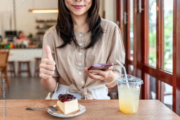 Fototapeta Young woman using smartphone to give a five-star satisfaction rating of the food and drinks at restaurant on social media