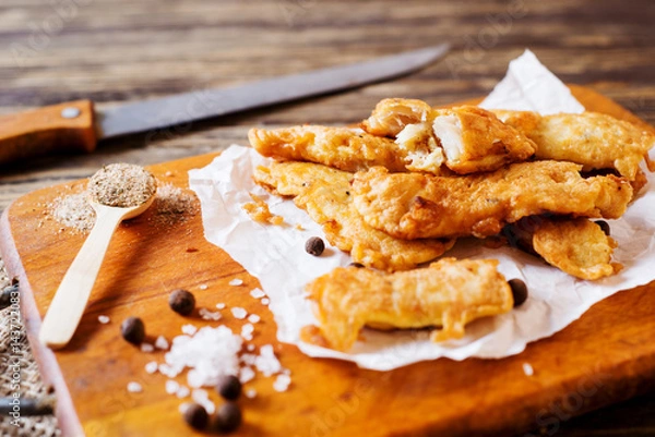 Fototapeta a fish. lunch or dinner, beer snack, fried hake fillets in batter, with spices, black pepper and salt on a wooden board, background