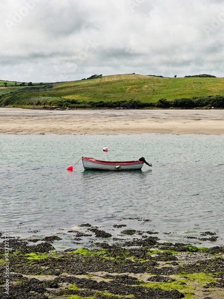 Obraz Tranquil Middle Ring Bay Beach in Ireland with a Small Boat Floating on Calm Waters.