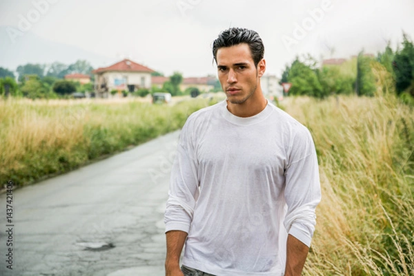 Fototapeta Man standing on a rural road with a serious expression and wet shirt
