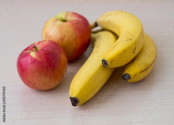 Fototapeta Two apples and bananas on a light wood background.