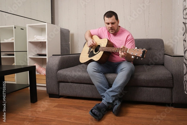 Fototapeta Musician Practicing Guitar at Home While Sitting on Sofa, Creating Relaxing and Casual Atmosphere