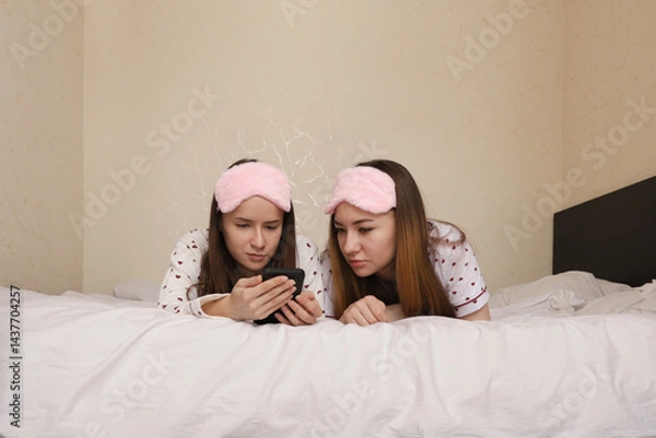 Fototapeta Close-up of female friends smiling and using mobile phone on white bed, showcasing digital lifestyle