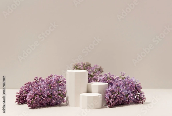 Obraz Elegant minimalistic spring-themed product display with white geometric pedestals surrounded by fresh lilac flowers on soft neutral background. Studio photography.