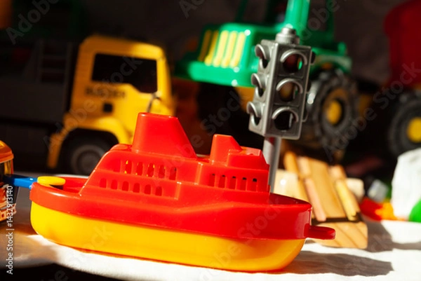 Obraz Vibrant toy still life: A red and yellow boat takes center stage among toy trucks and a traffic signal, creating a colorful play scene.