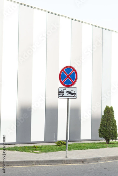 Fototapeta No stopping sign with towing symbol against a modern architectural backdrop, symbolizing traffic regulation and urban planning.