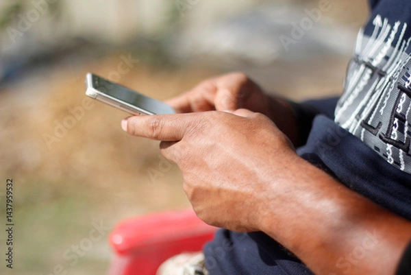 Fototapeta A man is holding a mobile phone with his both hand and blurred background