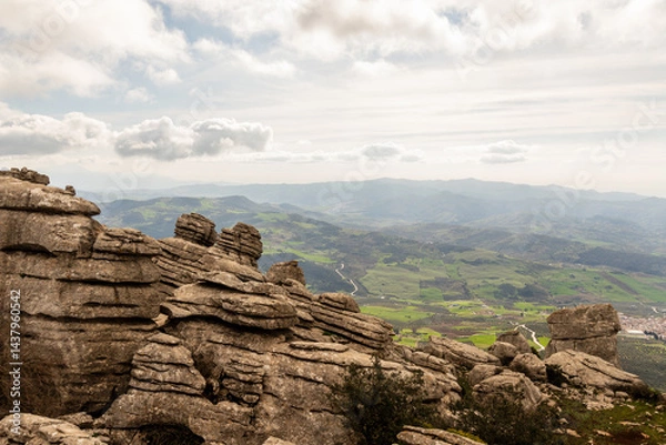 Obraz Scenic rocky landscape view from El Torcal de Antequera, Spain. Unique limestone rock formations overlooking green valleys and distant mountains under a partly cloudy sky in Antequera, Spain